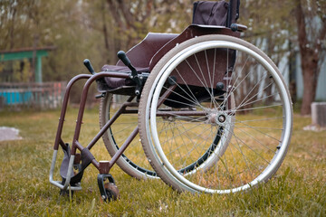 Empty wheelchair standing on grass in hospital park waiting for patient services. Invalid chair for disabled people parked outdoor in nature. Handicap accessible symbol. Health care medical concept