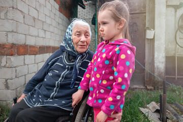 
Little baby girl and very old woman in a wheelchair. Little child hugging grandmother. Granddaughter. Youth and old age