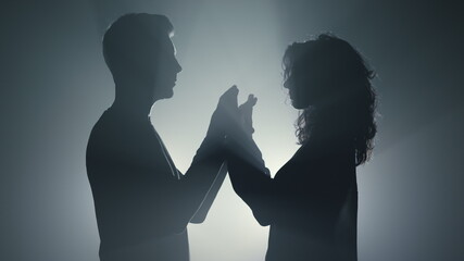 Sensual couple silhouette holding hands indoors. Lovers standing in dark space