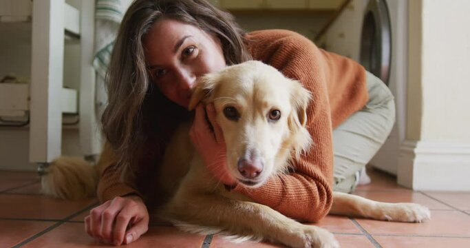 Smiling caucasian woman kissing and cuddling her pet dog sitting on floor at home
