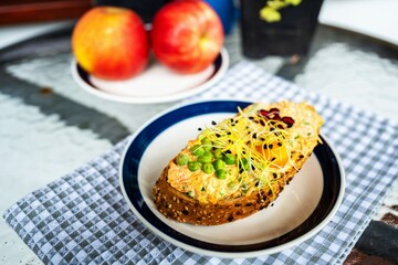 Toast with carrot spread, sprouts, pomegranate seed and egg on plate, 2 apple on table.