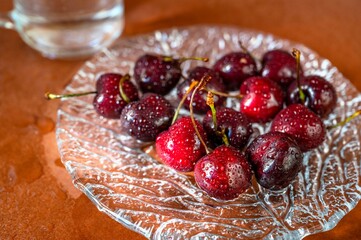 Dewy cherry on decorative glass plate, glass of water on brown .