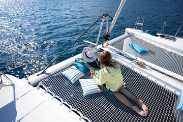 Two girls laying on the net of the sailing catamaran yacht - obrazy, fototapety, plakaty