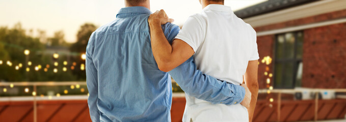 lgbt, homosexuality and people concept - close up of happy male gay couple or friends hugging from back over roof top party background