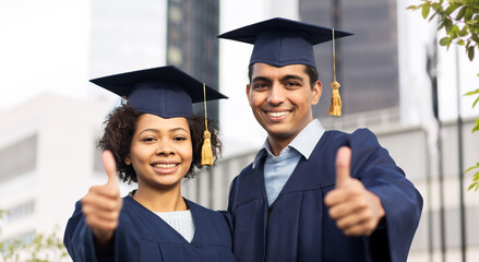 education, graduation, gesture and people concept - happy international students in mortar boards and bachelor gowns showing thumbs up over city background