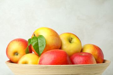Bowl with red apples on white textured background, close up
