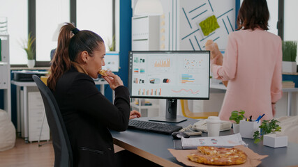 Closeup of businesswoman eating tasty pizza while analyzing financial statistics at desk in...