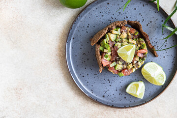 Raw tuna and avocado tartar served with rye bread crackers and lime on black ceramic plate. Gourmet fish tartar. Top view.