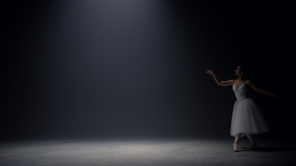 Sensual ballerina jumping on stage. Ballet dancer dancing pointe shoes indoors.