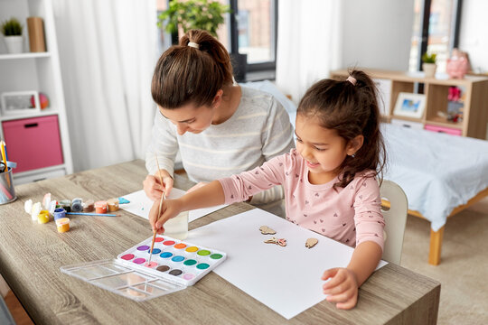 family, motherhood and leisure concept - mother spending time with her little daughter with colors painting chipboard items at home