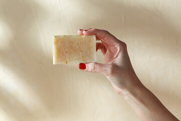 natural cosmetics, hygiene and beauty concept - hand holding bar of craft soap on beige background - obrazy, fototapety, plakaty