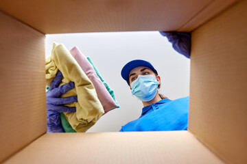 home delivery, shipping and pandemic concept - woman in protective medical mask and gloves packing clothes to parcel box