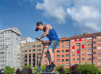 Young ride with scooter at skate park outdoors with blue sky in summer. 