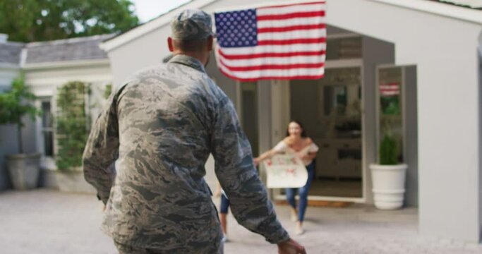 Caucasian male soldier greeting happy son and wife with welcome home sign outside their house