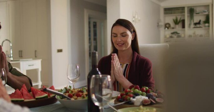 Smiling caucasian mother sitting at table in prayer before family meal