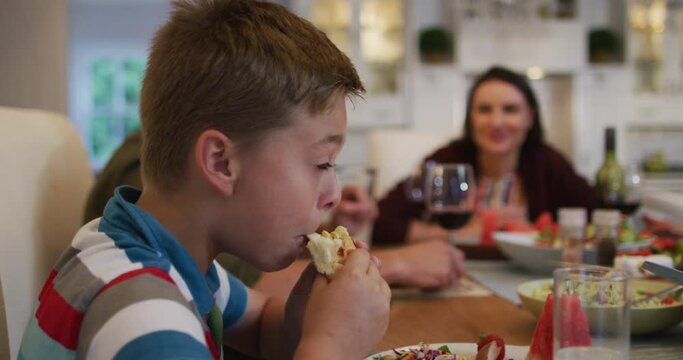 Smiling caucasian son eating at table during family meal, parents in background