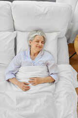 old age and people concept - happy senior woman sleeping in bed at home bedroom