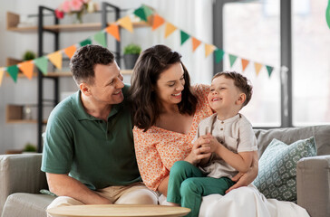 family, holidays and people concept - portrait of happy mother, father and little son sitting on sofa at home party