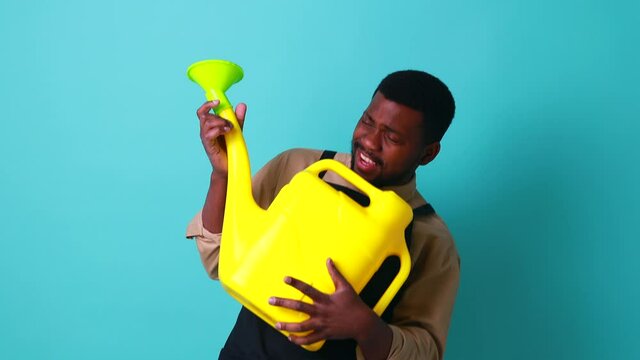 latino spain man in black apron holding yellow watering can in blue studio and playing like on guitar