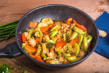 Vegetarian dish of broccoli, zucchini, onions and tomato in a skillet. Vegetables are stewed in a wok. Frying pan with vegetables on the table, top view