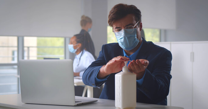 Young businessman in safety mask cleaning hands before working on computer in office - Powered by Adobe