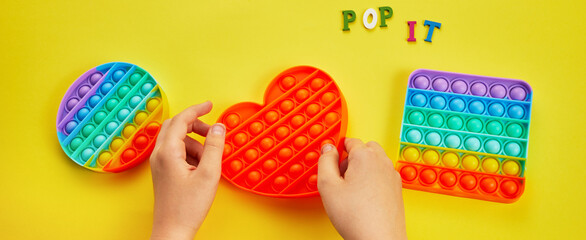 Kid hands playing with colorful pop It fidget toy. Colorful antistress sensory toy fidget push pop it. - obrazy, fototapety, plakaty