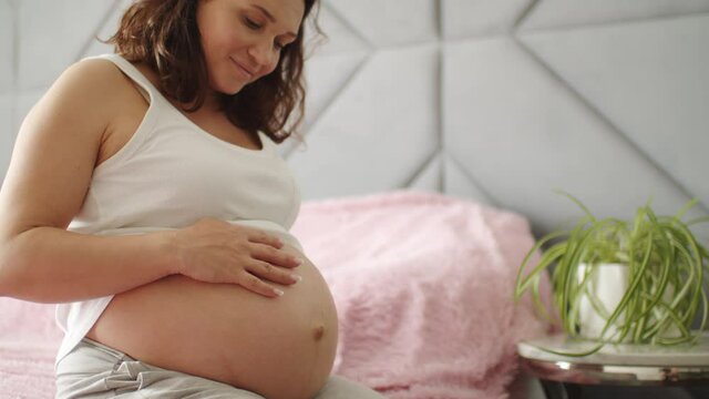 Happy pregnant woman expecting baby. Pregnant woman feeling happy at home while taking care of her child. Woman pregnancy concept and maternity prenatal care. Young expecting mother.  Slow motion.