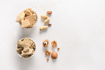 Sweet peanuts, walnuts halva in white bowls on white vertical background. View from above. Copy space.