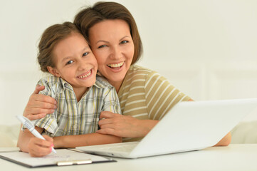 Cute girl and mother using laptop at home at desk