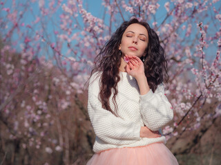 A beautiful young woman near a blooming spring pink tree