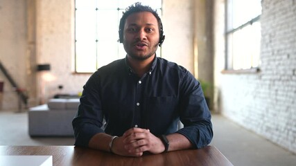 Smiling young indian office worker wearing headset looking and talking at the camera, positive mixed-race man working in the customer service department, holding video call
