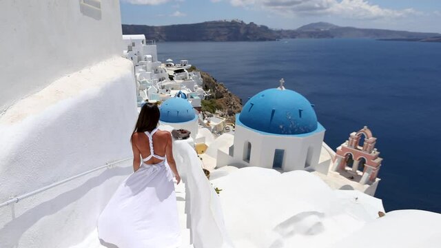 A woman in a white dress walks through the whitewashed houses of  Oia at Santorini island, Cyclades, Greece, during her summer holidays