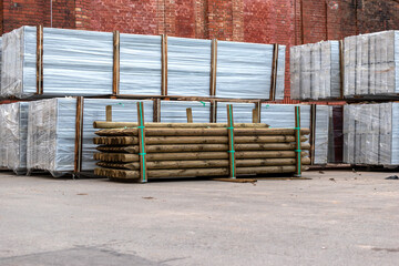 Material for protective wall stacked in the yard outdoors. Heaps of wooden fence posts, white protective fence panels.