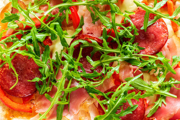 Top view of baked dish with arugula, bacon, cheese, pepper, salami, onion.