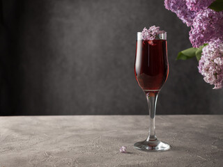 A full glass of red wine on a concrete table. Table decoration - lilac with purple flowers and green leaves. Lilac flowers in a glass. Aperitif concept. Dark background. Copy space.