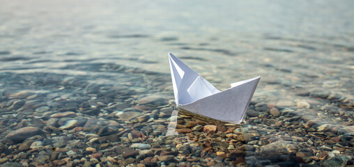 White paper boat in the clear water of large lake with a stony bottom