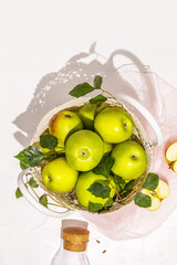 Vertical composition with green apples in a wicker bag and bottle with juice on a white background. Concept of local market and farm fruits. Apple picking and production of natural apple juice