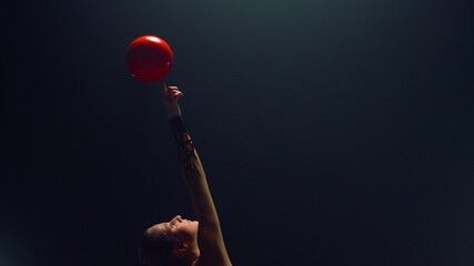 Gorgeous woman spinning ball on raised finger. Rhythmic gymnast exercising.