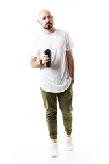 Handsome stylish bald young man walking holding water or coffee container. Full body length isolated on white background