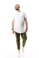 Fototapeta premium Cool confident shaved bearded stylish young man walking and looking away. Full body length isolated on white background
