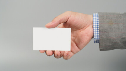 Hand is holding white blank card and wear suit on gray background. business man concept