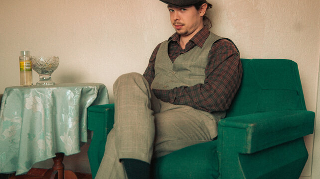 man in vintage suit is sitting on sofa and holding coffee cup. an old house. old colors. vintage background
