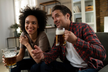 Boyfriend and girlfriend drinking beer at home. Happy couple watching sports game on tv..