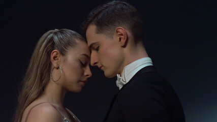 Ballroom couple standing in dark background. Young dancers looking each other.