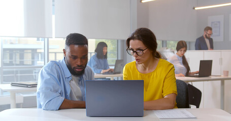 Diverse colleagues at office discussing and looking at laptop screen