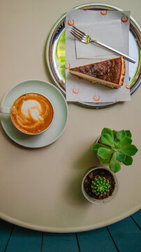 A cup of cappuccino, a slice of cheesecake on a beautiful table. A beautiful design with distant flowers.