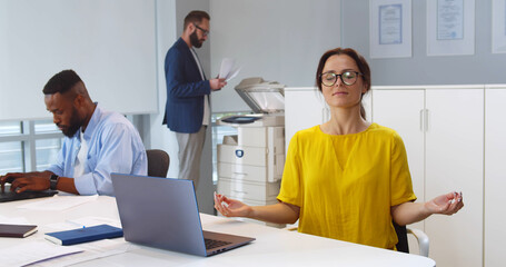 Calm mindful businesswoman meditating at office desk with eyes closed