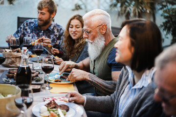 Family people eating at barbecue dinner - Multiracial friends enjoying meal outdoor - Food, friendship, gathering and summer lifestyle concept - Focus on hipster man face