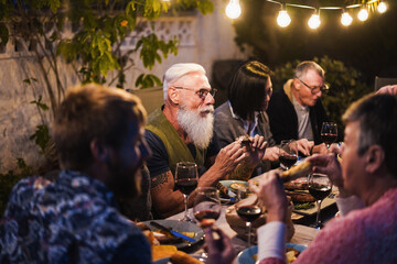Obraz premium Family people eating at home dinner - Multiracial friends enjoying meal outdoor - Food, friendship, gathering and summer lifestyle concept - Focus on hipster man face