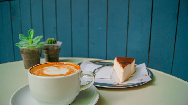 A cup of cappuccino, a slice of cheesecake on a beautiful table. A beautiful design with distant flowers.